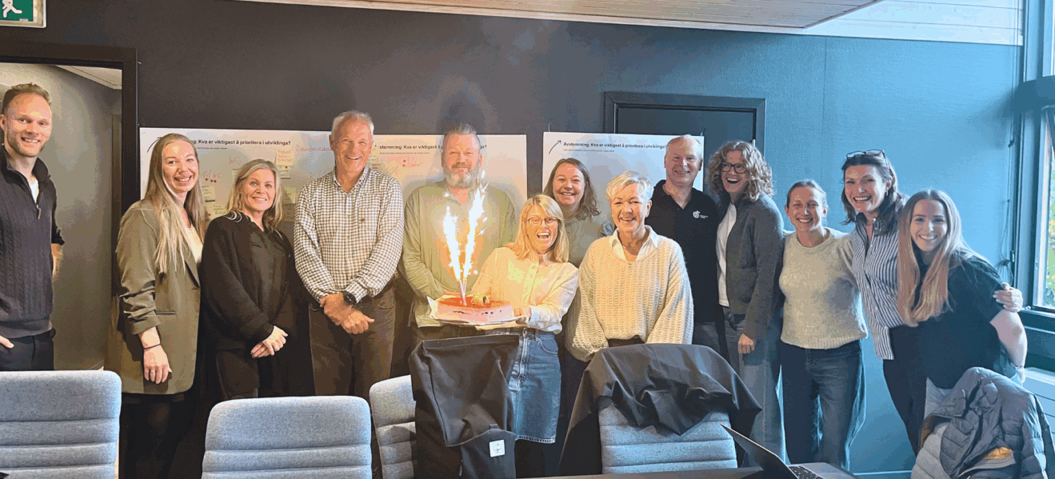Foto: Deltakarar på workshop står oppstilt og smilar. Prosjektleiar held ei kake med kakelys i handa.